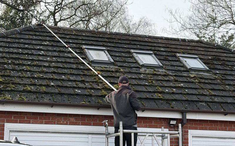 Josh cleaning a mossy concrete tile roof in Staffordshire from a tower, working the pitch with a long reach pole