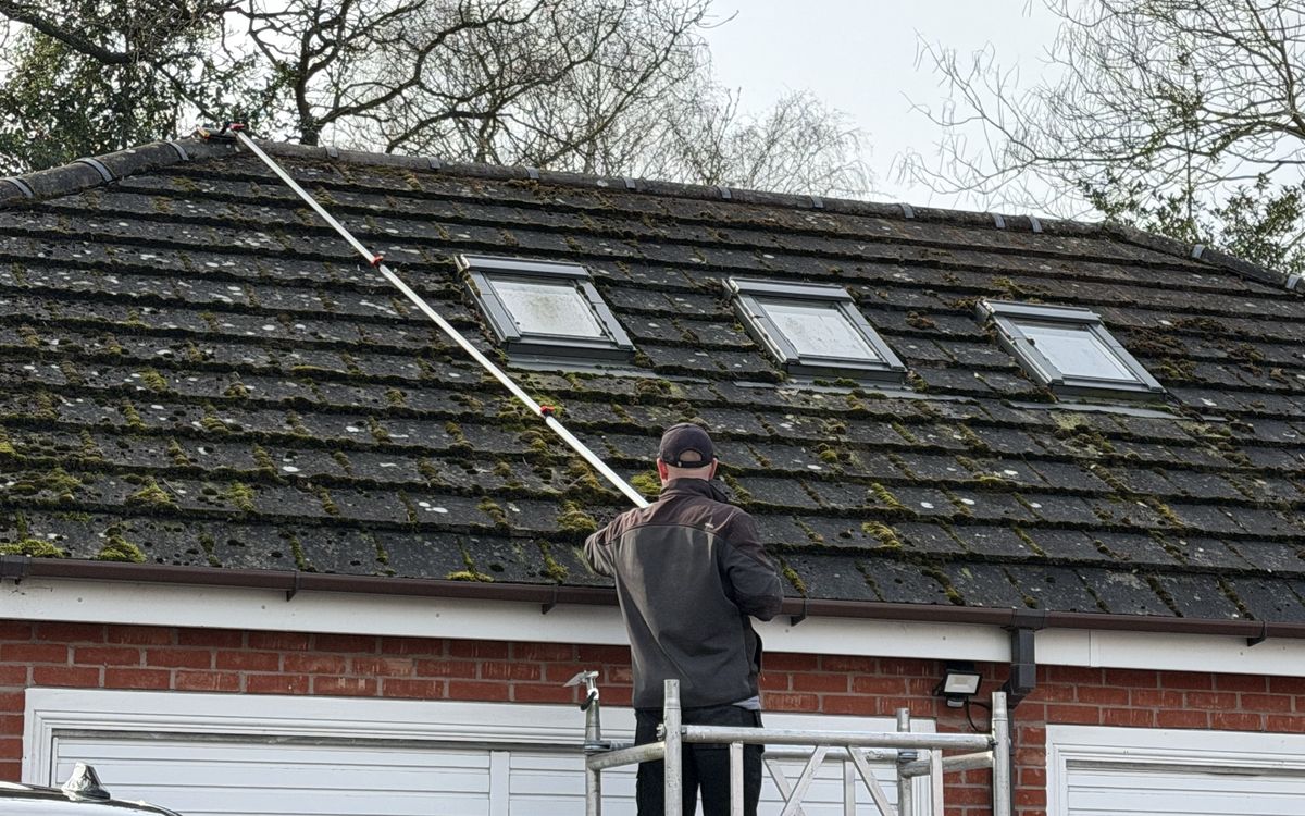 Josh cleaning a mossy concrete tile roof in Staffordshire from a tower, working the pitch with a long reach pole