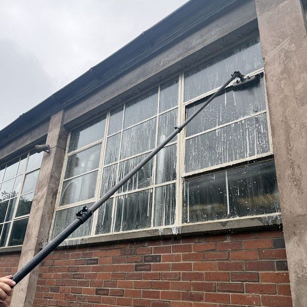 Metal framed factory windows being washed with a pole, seen from below