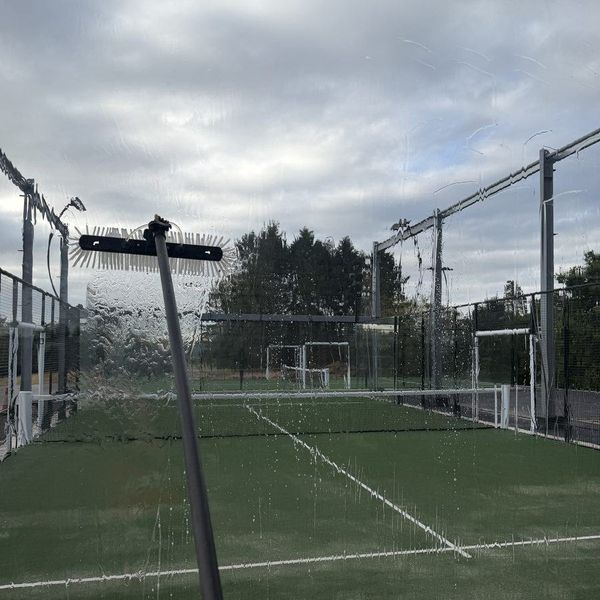 Cleaning the glass of a padel court, with water running down the pane