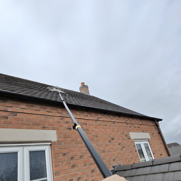 Cleaning a roof window with a water fed pole reaching up the slope of the roof
